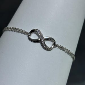 May include: A silver infinity symbol bracelet with small clear stones set into the symbol. The bracelet has a delicate chain.