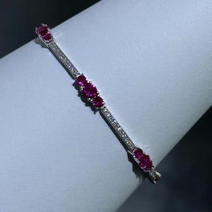 Op de afbeelding: Een zilveren armband met een rij kleine, heldere diamanten en drie grotere, ovale robijnstenen.