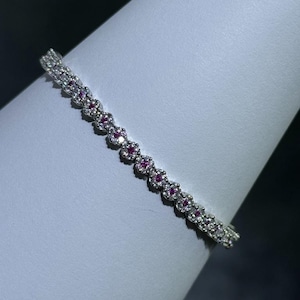 May include: A silver bracelet with a row of small pink and white gemstones.