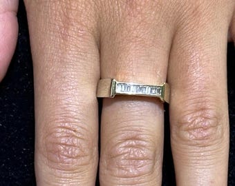 May include: A gold band ring with a row of small, rectangular diamonds set in a channel setting.