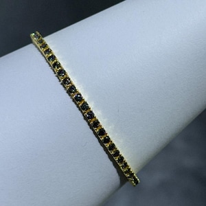 May include: A gold bracelet with a row of small, black, iridescent stones.