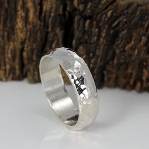 May include: A silver hammered wedding band with a smooth interior. The band is thick and has a textured, hammered finish.