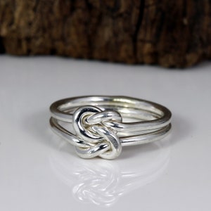 May include: A silver ring with a knot design. The knot is made of three strands of silver wire that are intertwined.