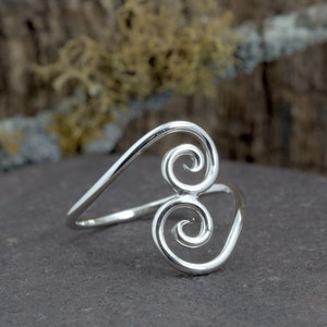 May include: A silver ring with a double spiral design. The ring is made of sterling silver and is a simple, elegant piece of jewelry.
