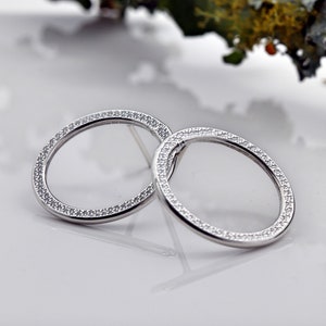 May include: A pair of silver hoop earrings with a circle of small clear stones around the edge.
