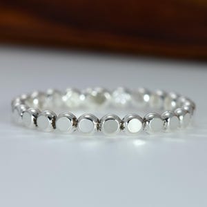 May include: A silver ring featuring a series of small, round, polished beads. The ring is made of a shiny, reflective metal, and the beads are evenly spaced around the band. The ring is shown on a white surface.
