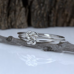 May include: A silver ring with a knot design. The ring is made of two bands that are intertwined.