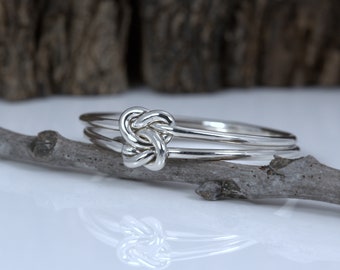 May include: A silver ring with a knot design. The ring is made of two bands that are intertwined.