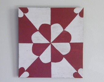 May include: Square canvas art with a geometric design. The artwork features a pattern of white and burgundy shapes, including triangles and heart-like forms. The design is symmetrical and centered, creating a visually balanced composition.