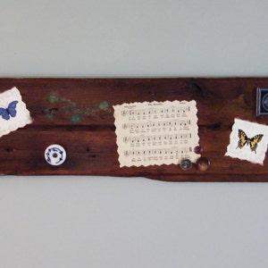 May include: A rustic wooden sign with a blue butterfly, a yellow butterfly, a sheet of music, a small white knob, and a small metal box.