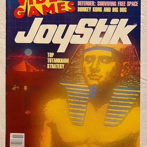 Peut inclure: Une couverture de magazine représentant une illustration jaune et orange d'un pharaon avec le titre "JoyStik" et le texte "Comment gagner aux jeux vidéo". La couverture du magazine comprend également le texte "Isaac Asimov sur l'avenir", "Defender : Survivre dans l'espace libre", "Donkey Kong et Dig Dug", et "Stratégie du Top Toutankhamon".