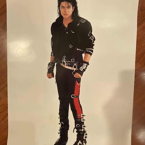 May include: A black leather jacket with silver buckles and a red stripe down the side of the pants. The person is wearing black boots with silver buckles.
