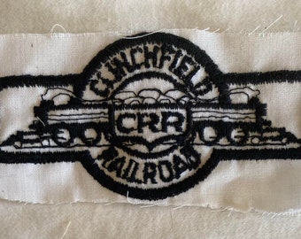 May include: Black and white embroidered patch featuring a train engine with the text "Clinchfield Railroad" and "CRR" in a circle.