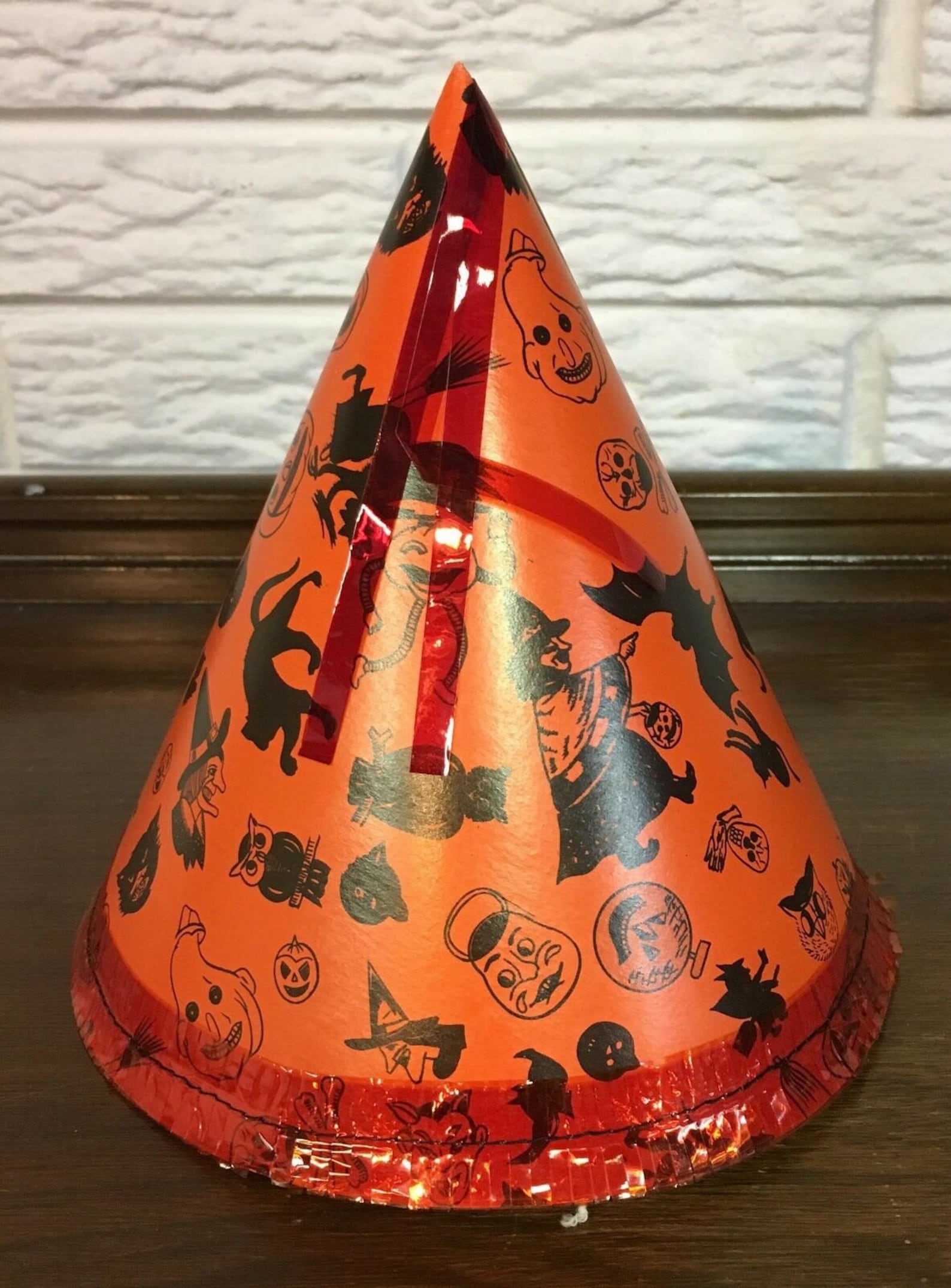 A Vintage Scene Wrapped Around the Cone Orange vintage cardboard Halloween cone hat with dark illustrated figures.