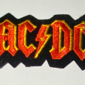 Op de afbeelding: Een zwarte strijk-op patch met de bandnaam "AC/DC" geborduurd in rood en geel garen.