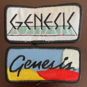 May include: Two embroidered patches featuring the word "Genesis" in black lettering. The top patch is white with a blue and pink striped design. The bottom patch is blue with a yellow and red design.