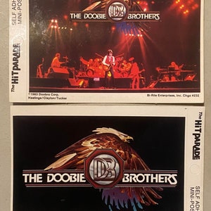 May include: Two vintage self-adhesive mini-posters featuring The Doobie Brothers. The top poster shows the band performing on stage with a red, white, and blue eagle logo. The bottom poster features a close-up of the eagle logo with the band's name.