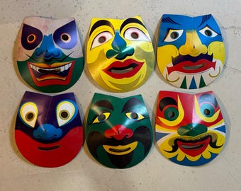 Puede incluir: Seis máscaras faciales coloridas y estilizadas con diversas expresiones. Cada máscara presenta una combinación única de colores, incluyendo rojo, amarillo, azul y verde. Las máscaras tienen aberturas para los ojos y la boca, y probablemente son para disfraces o decoración.