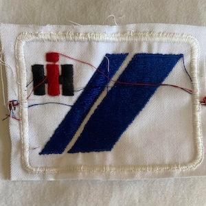 May include: A white embroidered patch with a blue and red logo. The logo features the letters "IH" in red and black with a blue diagonal stripe.