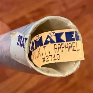 May include: A rolled-up item with a label that reads "STAR & MAKE" and "M.N.T. RAPHAEL #2710". The label has blue and white text and a star graphic. The item is wrapped in a white tube.