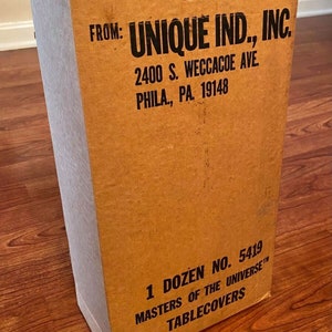 Może przedstawiać: Brązowe kartonowe pudełko z nadrukiem "FROM: UNIQUE IND., INC. 2400 S. WECCACOE AVE. PHILA., PA. 19148 1 DOZEN NO. 5419 MASTERS OF THE UNIVERSE TABLECOVERS".
