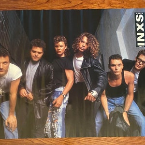 May include: A vintage poster featuring the band INXS with the album title "Kick" printed in red and white stars. The band members are dressed in casual clothing and are standing in an urban setting.