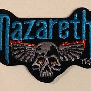 May include: Black embroidered patch with the band name "Nazareth" in blue lettering and a winged skull with flames in red and yellow.