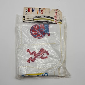 May include: A white inflatable swim vest in a clear plastic package. The vest has red and blue graphics. The packaging includes the text "SWIM VESTO" and "AN ALVIMAR PRODUCT".