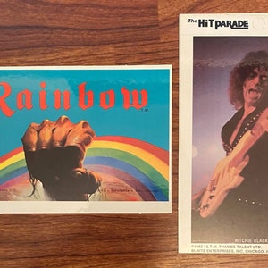 Könnte beinhalten: Ein vintage Mini-Poster mit Selbstklebefunktion, das einen Regenbogen und eine Faust mit dem Wort "Rainbow" in roten Buchstaben zeigt. Das Poster stammt von The Hit Parade.