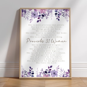 May include: A framed print featuring the text of Proverbs 31 Woman, with a floral design in shades of purple and lavender. The print has a light wood frame and is suitable for home decor.