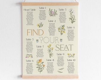 May include: A wedding seating chart printed on cream-colored paper, featuring floral illustrations and the words "Find Your Seat." The chart is displayed on a wooden frame and suspended by a natural twine cord.