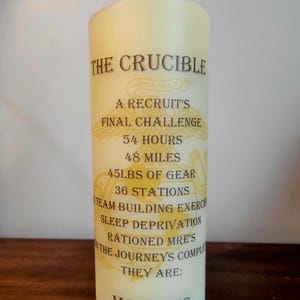 May include: A cream-colored pillar candle with text that reads "THE CRUCIBLE" and details of a Marine recruit's final challenge, including 48 miles, 45lbs of gear, and 36 stations. The word "MARINES" is at the bottom.