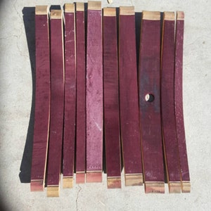 May include: Ten pieces of reclaimed wine barrel wood, each approximately 30 cm long and 5 cm wide. The wood is a deep burgundy red colour with a natural wood grain. The ends of the wood are trimmed with a thin strip of natural wood.