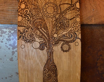 Puede incluir: Una tabla de barril de vino de madera con un diseño decorativo de una botella y un patrón floral quemado en la madera. La tabla tiene bandas metálicas con remaches alrededor de la parte superior e inferior.
