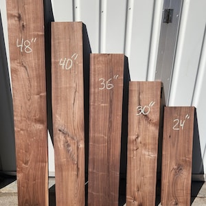 May include: Five rectangular, unfinished wood planks of varying lengths. The planks are a rich brown color with visible wood grain. The lengths are marked in white: 48", 40", 36", 30", and 24".