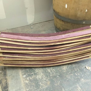 May include: A stack of curved wooden barrel staves with a pink sealant between each stave.