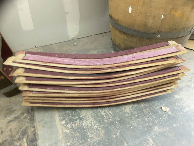 May include: A stack of curved wooden barrel staves with a pink sealant between each stave.
