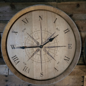 May include: A wooden clock with Roman numeral markings and a compass design in the center. The clock face is light brown with dark brown markings. The clock hands are black.