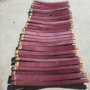 May include: A stack of 15 wine barrel staves, each with a curved shape and a reddish-brown color. The staves are arranged in a row, with the top stave slightly overlapping the one below it.