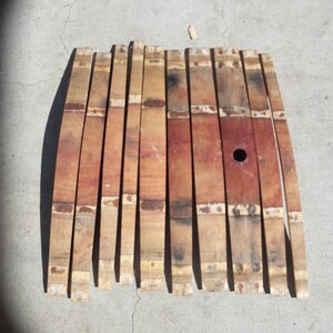 May include: A set of 12 wooden barrel staves, each with a slightly curved shape and a metal band. The staves are a mix of light and dark brown wood with a reddish hue.