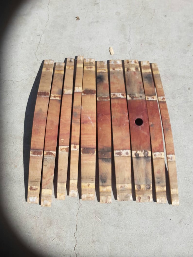 May include: A set of 12 wooden barrel staves, each with a slightly curved shape and a metal band. The staves are a mix of light and dark brown wood with a reddish hue.