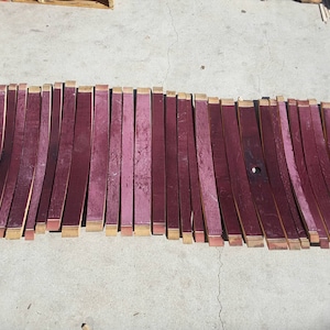 May include: A collection of approximately 30 wine barrel staves, each about 24 inches long, arranged in a row. The staves are a deep reddish-brown color and have a slightly curved shape.