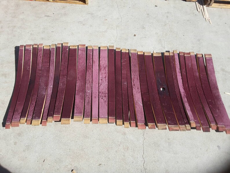 May include: A collection of approximately 30 wine barrel staves, each about 24 inches long, arranged in a row. The staves are a deep reddish-brown color and have a slightly curved shape.