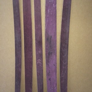 May include: Five wooden wine barrel staves, each with a slightly different shade of purple, are arranged horizontally on a brown surface. The staves are all approximately the same length and width.