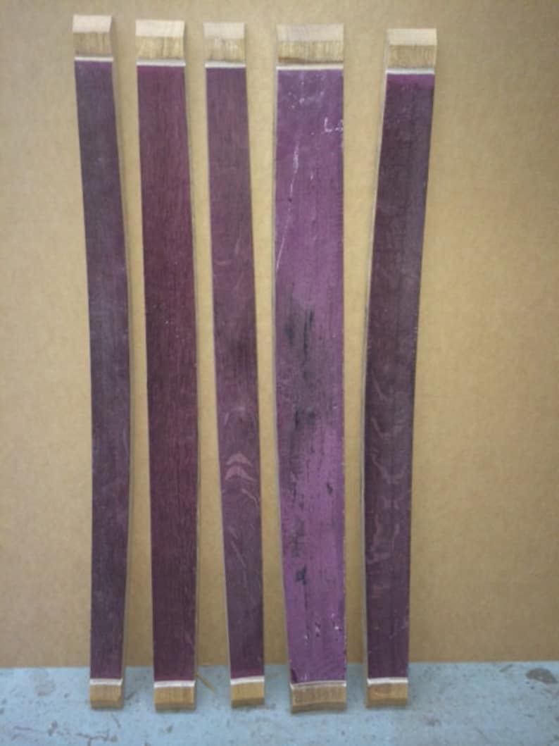May include: Five wooden wine barrel staves, each with a slightly different shade of purple, are arranged horizontally on a brown surface. The staves are all approximately the same length and width.