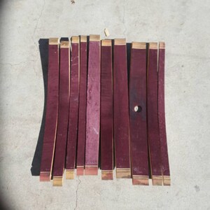 May include: A set of 12 wine barrel staves, each approximately 45 cm long, with a reddish-brown colour and a natural wood finish. The staves are arranged in a row on a concrete surface.