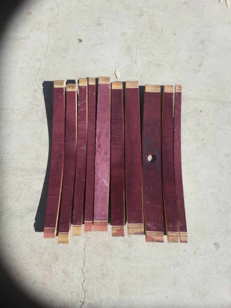 May include: A set of 12 wine barrel staves, each approximately 45 cm long, with a reddish-brown colour and a natural wood finish. The staves are arranged in a row on a concrete surface.