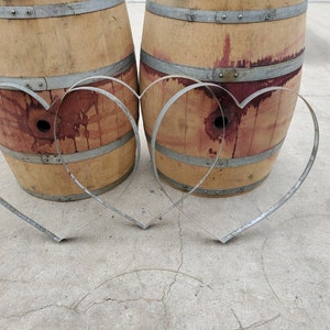 May include: Two wooden wine barrels with metal hoops, each with a metal heart-shaped hoop in front of them.