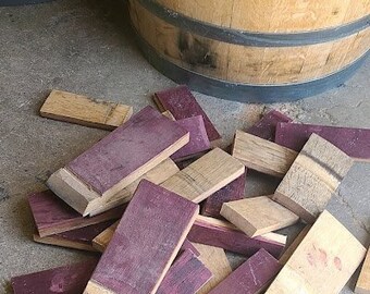 May include: A pile of wooden wine barrel staves, some are natural wood color and some are stained a deep purple.