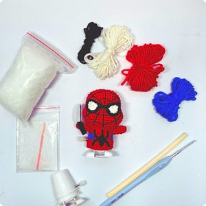 May include: A crochet kit featuring a red and black Spider-Man figure, with white eyes and a black web design. The kit includes various colored yarns, stuffing, a crochet hook, and other crafting supplies. The kit is designed for making a small, handmade toy.